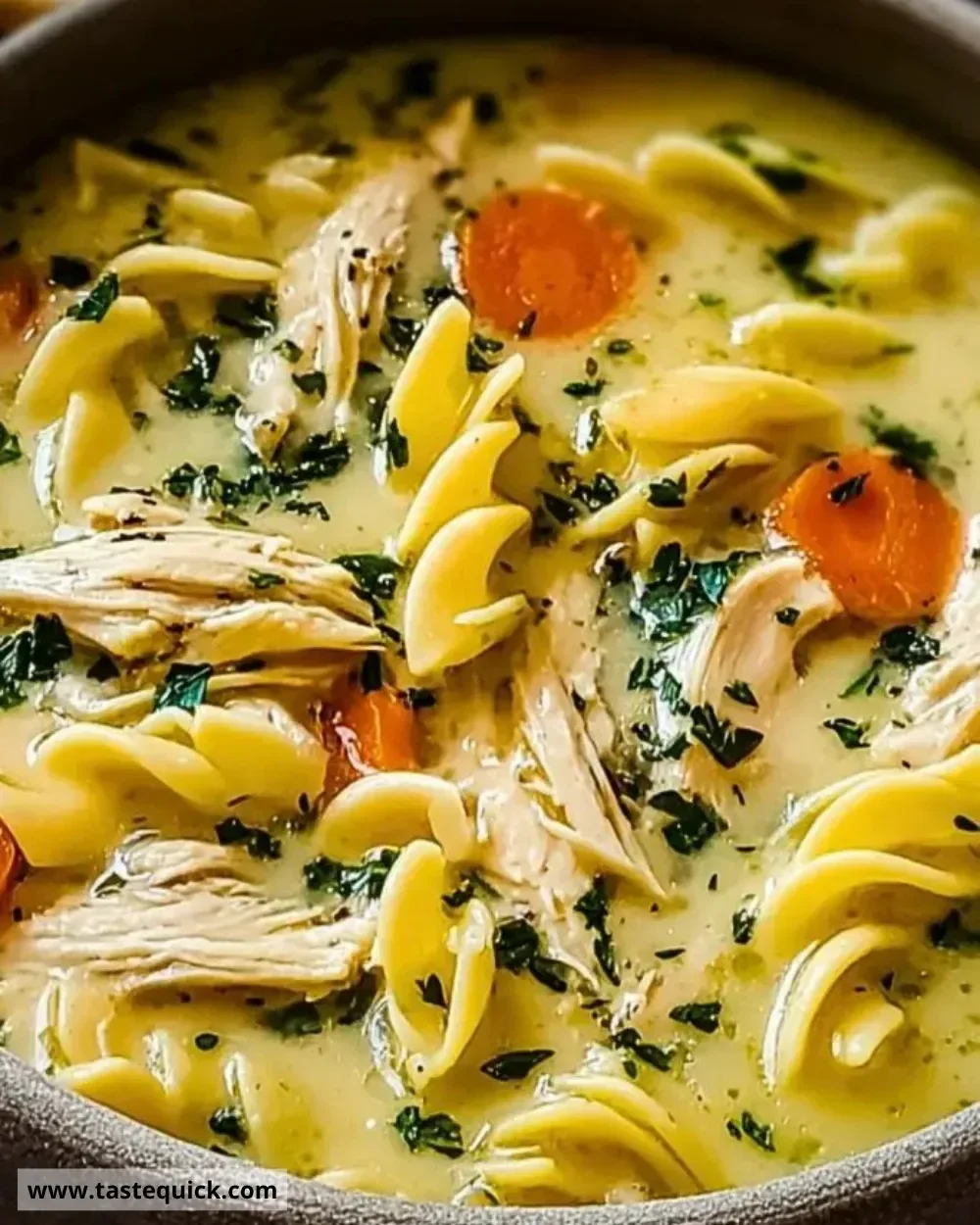 Bowl of creamy chicken noodle soup garnished with herbs.