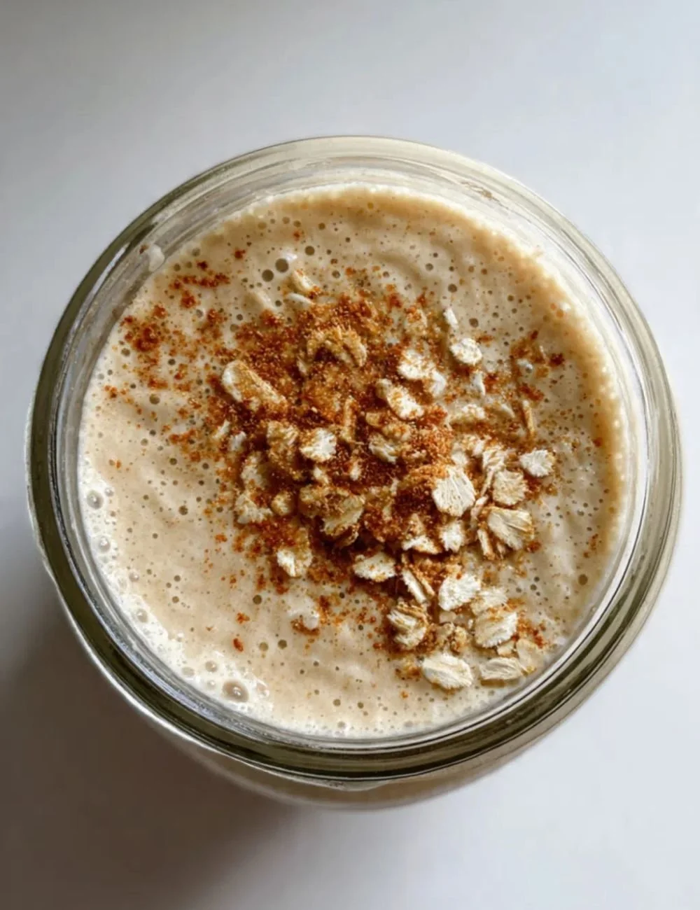 Banana Oat Smoothie with cinnamon in a glass, topped with banana slices