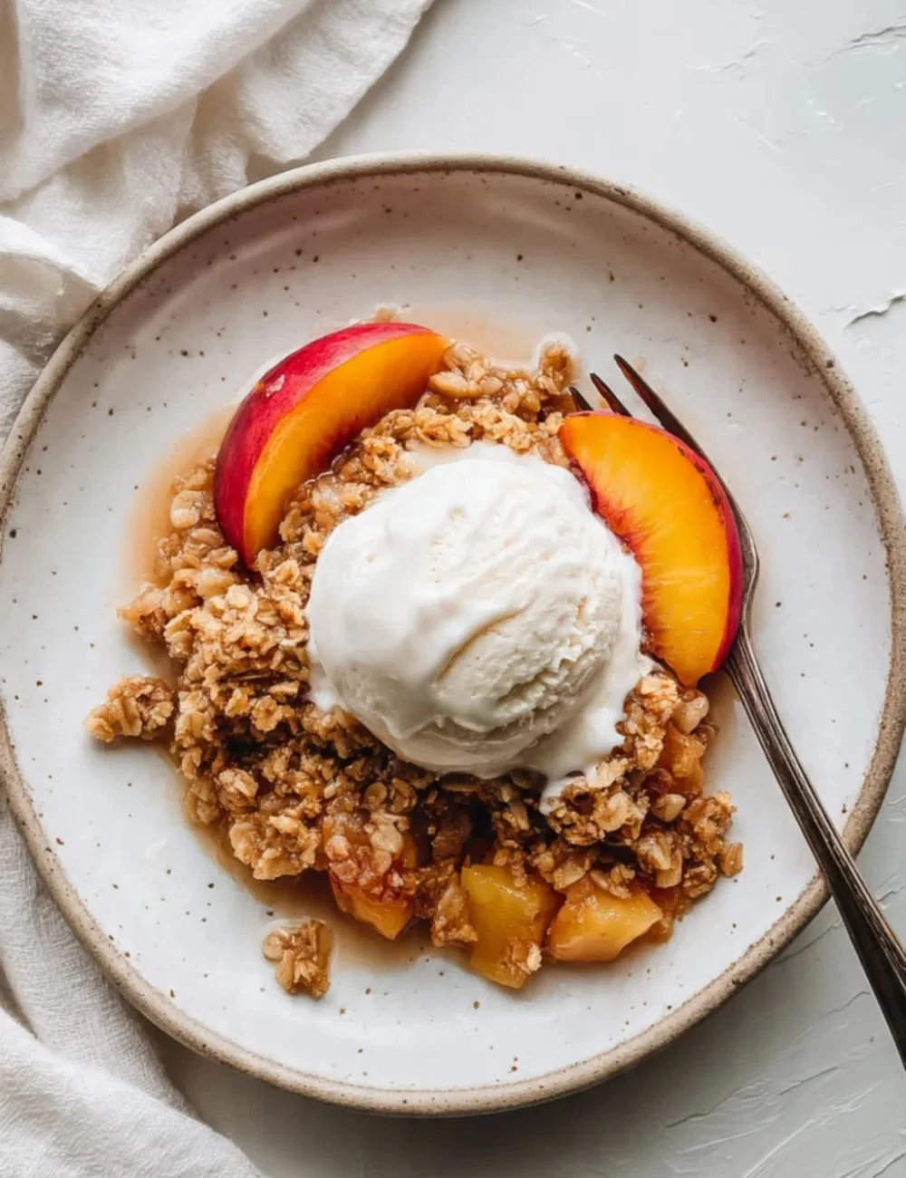 A bowl of healthy peach crisp topped with oats and almonds, served with vanilla ice cream.