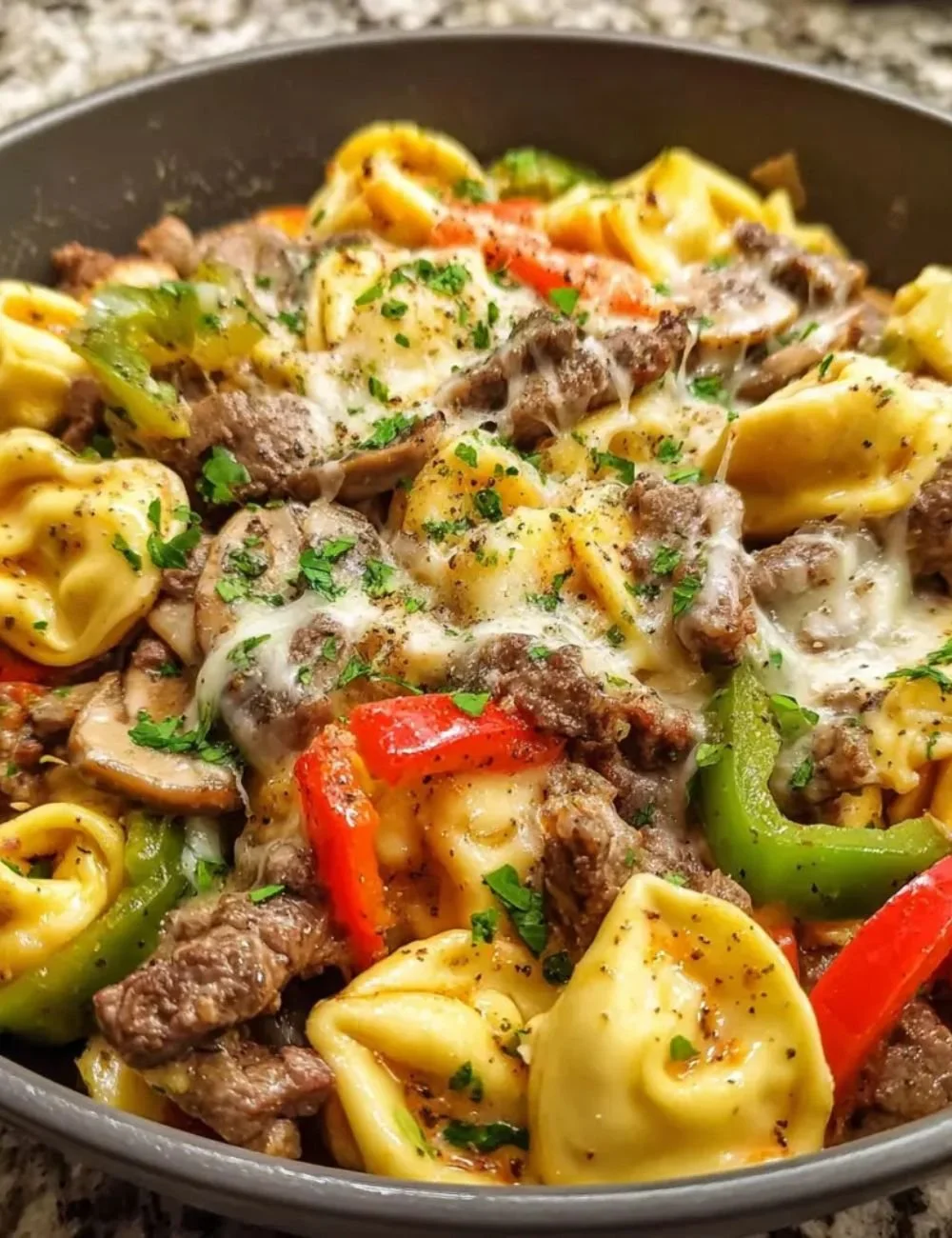 Crock Pot Cheesesteak Tortellini, a tasty dish served in a bowl with melted cheese.