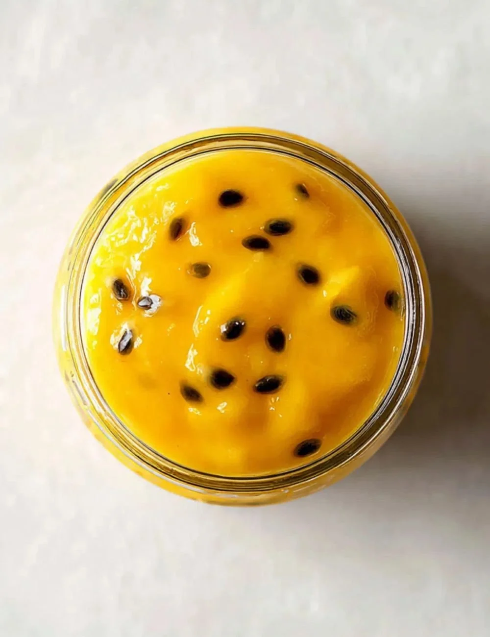 Delicious and vibrant Passionfruit Curd in a glass jar on a wooden table.